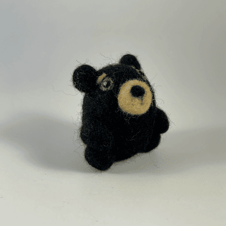 A small round needle-felted black bear faces 1/4 towards the right.