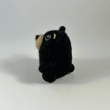 A small round needle-felted black bear faces towards the left.