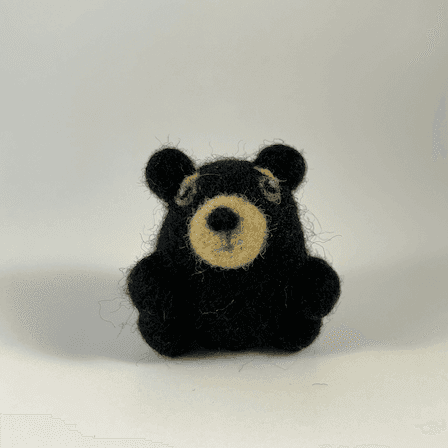 A small round needle-felted black bear faces directly towards the camera.