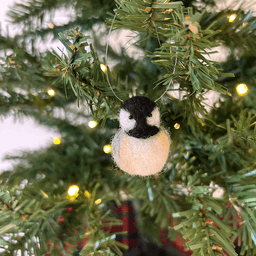 A close up of a needle-felted black-capped chickadee hanging from a Christmas tree, facing directly towards the camera.