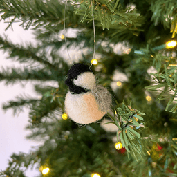 A close up of a needle-felted black-capped chickadee hanging from a Christmas tree, facing 1/4 to the left.