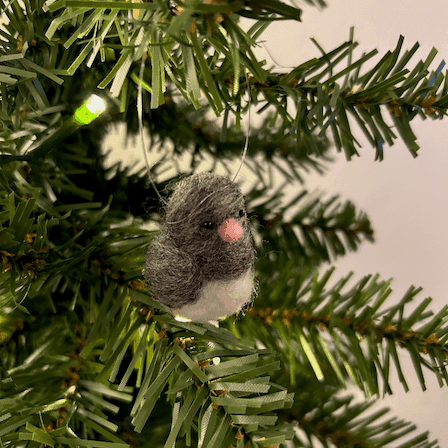 A close up of a needle-felted dark-eyed junco ornament, hanging on a tree, facing 1/4 to the right.