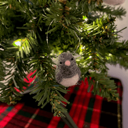 A close up of a needle-felted dark-eyed junco ornament, hanging on a tree, facing towards the camera.