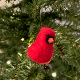 A close up of a needle-felted Northern cardinal ornament hanging on a tree, facing 1/4 to the right.