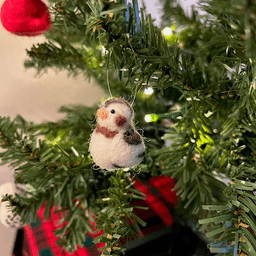 A close up of a needle-felted snow bunting ornament hanging on a tree, facing directly towards the left.