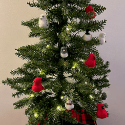 A small artificial Christmas tree with white lights sits on a red tartan pattern. The tree's ornaments are all borbs: two snowy owls,  four Northern cardinals, one black-capped chickadee, two snow buntings, and two dark-eyed juncos. The snow buntings are in the bottom center and obscured on the right just below the middle.