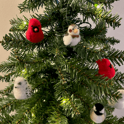 Close up of a small artificial Christmas tree with white lights. The tree's ornaments are all borbs: one snowy owl, one black-capped chickadee, two Northern cardinals, one snow bunting. The snow bunting is in the top right of center.