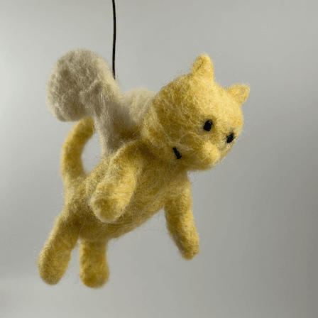 Silky the Catnary from the 13 Storey Treehouse series, needle felted with a yellow body, cream-colored wings, black round eyes, a round nose, a black half smile, and cat ears and cat tail. The catnary faces 3/4 towards the right.