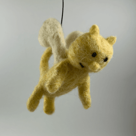 SIlky the Catnary from the 13 Storey Treehouse series, needle felted with a yellow body, cream-colored wings, black round eyes, a round nose, a black half smile, and cat ears and cat tail. The catnary faces 3/4 towards the right facing downwards.