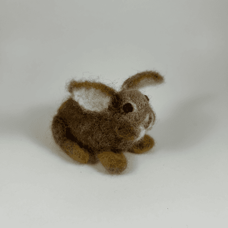 A needle-felted Eastern cottontail rabbit faces 3/4 towards the right. Its ears are splayed widely, showing the lighter colored undersides of the ears. Its cheeks are round and its large dark eyes bulbous.