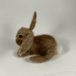 A needle-felted Eastern cottontail faces towards the left, showing its cotton puff tail.