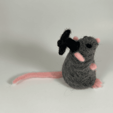 A grey rat with black eyes, pink nose, pink ears, pink paws and pink tail wearing a black graduation cap faces towards the right in profile, displaying its full tail length.