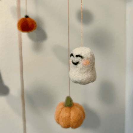 Close up of a Halloween baby mobile’s hanging items with a smiling ghost and pumpkins.