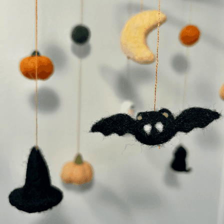 Close up of a Halloween baby mobile’s hanging items with  pumpkins, a bat, a witch’s hat, a crescent moon, and orange and green balls.