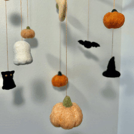 Close up of a Halloween baby mobile’s hanging items with pumpkins, a black cat, a bat, a witch’s hat, a ghost, and a crescent moon