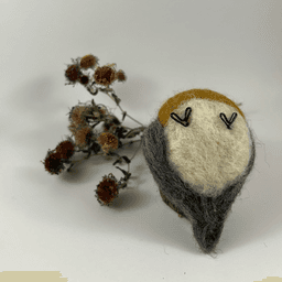 A needle-felted American Robin lies upturned showing its white bottom, black wire feets and grey underside of its tail. A dried spray of New England aster lies behind it.