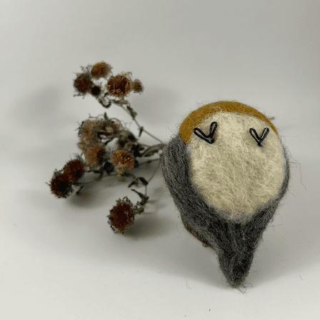 A needle-felted American Robin lies upturned showing its white bottom, black wire feets and grey underside of its tail. A dried spray of New England aster lies behind it.