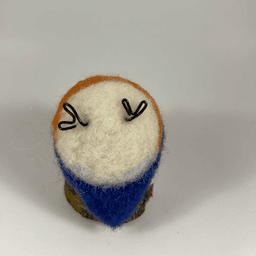 A needle-felted Eastern bluebird sits upturned revealing its flat white underside, royal blue tail and black wire feets.