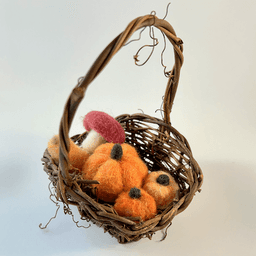 A small viney basket holds needle felted produce: a mushroom, a butternut squash, and three pumpkins of different shades of orange.