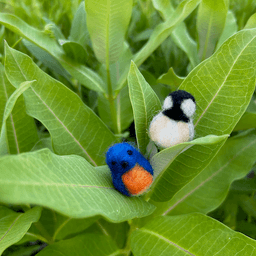 Four miniature needle-felted birds sit on two half-inch cross sections of a branch, sitting in alternating species: Eastern blue bird and black-capped chickadee. Two birds fit on each branch cut out. There is a spray of goldenrod in the background.