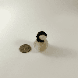 A miniature needle-felted black-capped chickadee borb sits next to a US penny.
