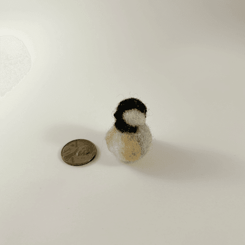 A miniature needle-felted black-capped chickadee borb sits next to a US penny.