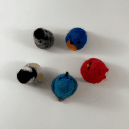 From overhead, five miniature needle felted borbs positioned in a circle face inward. From top right clockwise, a grey catbird, Eastern bluebird, Northern cardinal, Palestine sunbird, and black-capped chickadee.