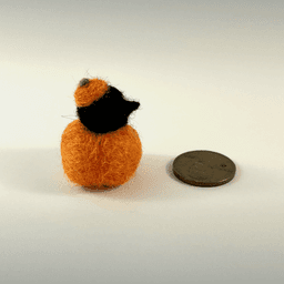 A tiny needle-felted black corvid borb pokes its head out of an orange pumpkin, wearing a pumpkin stem hat. The mini borb faces right next to a US penny.