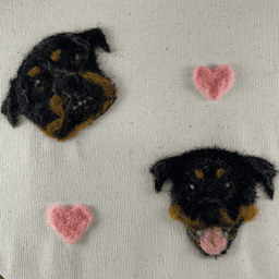 Close up of a wool painting of the faces of two rottweiler dogs, Vanya and Sheba. Vanya on the left is looking up with head tilted, hopeful. Sheba on the right is smiling with bright eyes and tongue out. There are pink hearts floating among them.