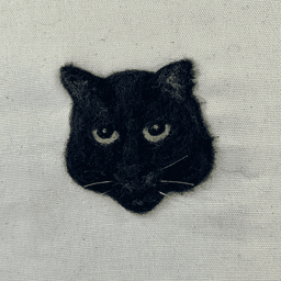 Close up of a needle felted portrait of a black cat with green eyes and a flat expression.