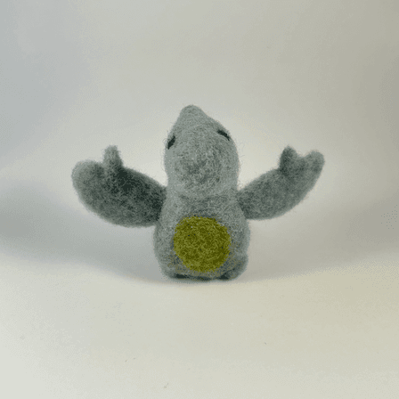 A needle-felted grey blue pterodactyl with a green tummy faces towards the camera.