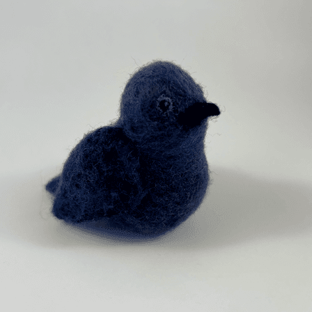 A needle-felted purple martin faces towards the right.