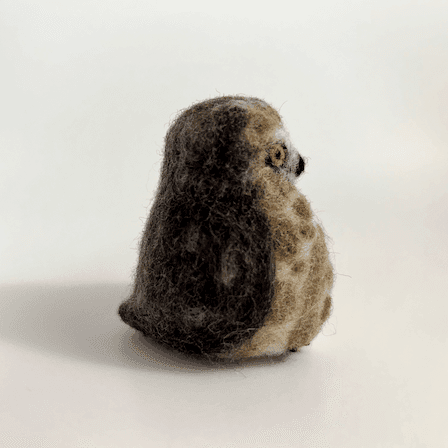 A needle-felted Northern saw-whet owl borb faces towards the right.