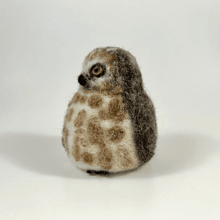 A needle-felted Northern saw-whet owl borb faces towards the left.