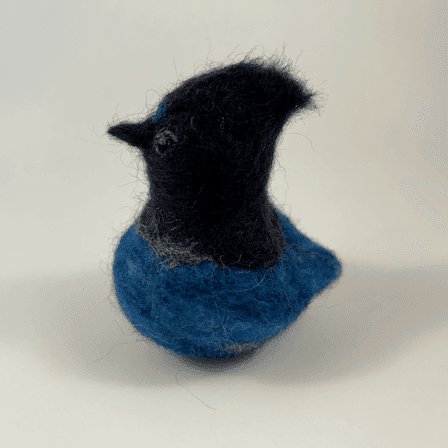 A needle-felted Steller's jay borb faces away from the camera towards the left.