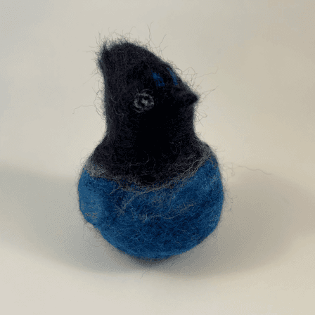 A needle-felted Steller's jay borb faces away from the camera 1/4 towards the right.