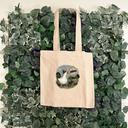 Canvas bag depicting a wizard goose honking hanging on a back drop of artificial ivy.