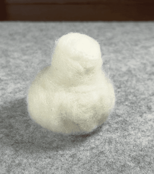 A completed borb base, sitting on a grey felting mat, slightly bumpy but a generic BB-8 or baby chick shape.