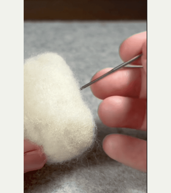 Close up of a right hand poking a felting needle into the bottom of a needle felted borb base.