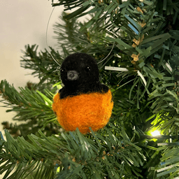 A close up of a needle-felted Baltimore oriole ornament, hanging on a tree, facing the camera.