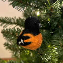 A close up of a needle-felted Baltimore oriole ornament, hanging on a tree, facing 1/4 to the right.