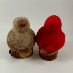 A pair of male and female Northern cardinals, scultped in needle felt, sit on half inch circle sections of branches, facing directly away from the camera. The female is a buff cream color with wine-stained wings, tail and crest. The male is a cardinal red color with grey detail on its tail. Their crests and tail points are short and round.