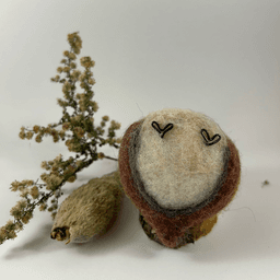 A female needle-felted Northern cardinal sits upturned revealing her flat strawberry blond underside, wine-stained wings with grey details underneath, and black wire feets.
